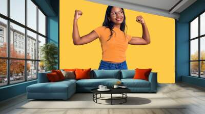 Young indian girl wearing casual clothes and glasses showing arms muscles smiling proud. fitness concept. Wall mural