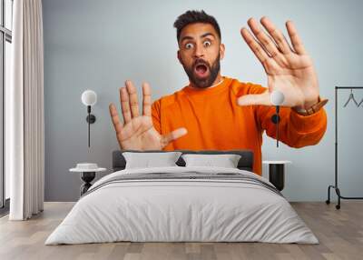 Young indian man wearing orange sweater over isolated white background afraid and terrified with fear expression stop gesture with hands, shouting in shock. Panic concept. Wall mural