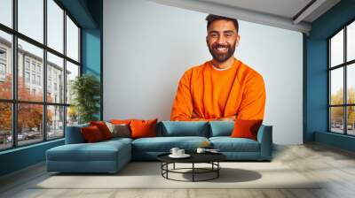 Young indian man wearing orange sweater over isolated white background happy face smiling with crossed arms looking at the camera. Positive person. Wall mural