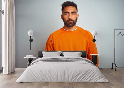 Young indian man wearing orange sweater over isolated white background Relaxed with serious expression on face. Simple and natural looking at the camera. Wall mural