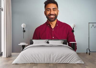 Young indian man wearing red elegant shirt standing over isolated grey background with hands together and crossed fingers smiling relaxed and cheerful. Success and optimistic Wall mural