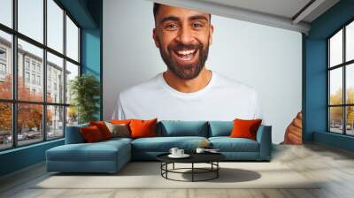 Young indian man wearing t-shirt standing over isolated white background celebrating surprised and amazed for success with arms raised and open eyes. Winner concept. Wall mural