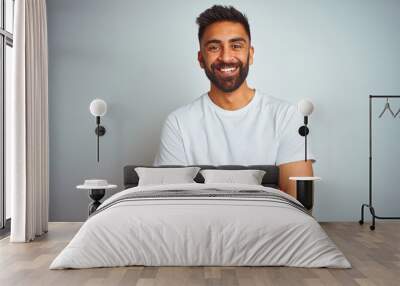 Young indian man wearing t-shirt standing over isolated white background happy face smiling with crossed arms looking at the camera. Positive person. Wall mural