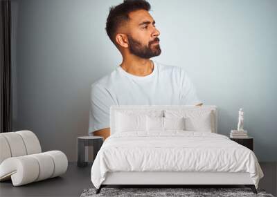 Young indian man wearing t-shirt standing over isolated white background looking to the side with arms crossed convinced and confident Wall mural