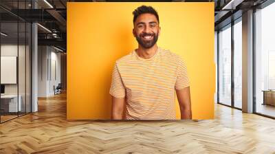 Young indian man wearing t-shirt standing over isolated yellow background with a happy and cool smile on face. Lucky person. Wall mural