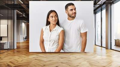 Young interracial couple standing together in love over isolated background smiling looking to the side and staring away thinking. Wall mural