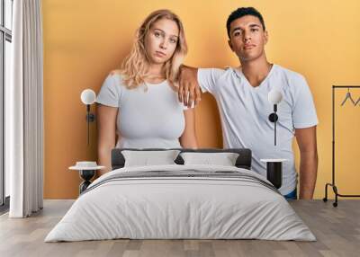 Young interracial couple wearing casual white tshirt relaxed with serious expression on face. simple and natural looking at the camera. Wall mural