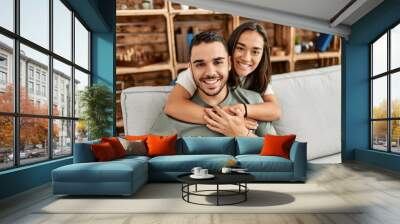 Young latin couple sitting on the sofa hugging at home. Wall mural