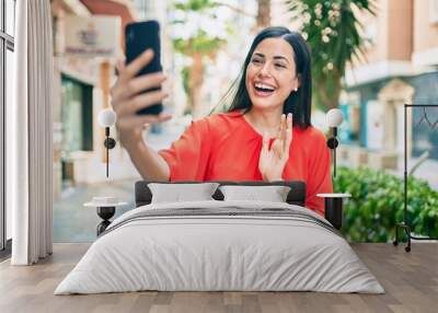 Young latin girl smiling happy doing video call using smartphone at the city. Wall mural