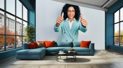 Young latin girl wearing business clothes and glasses approving doing positive gesture with hand, thumbs up smiling and happy for success. winner gesture. Wall mural