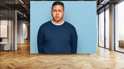 Young latin man wearing casual clothes puffing cheeks with funny face. mouth inflated with air, crazy expression. Wall mural