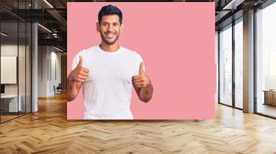 Young latin man wearing casual clothes success sign doing positive gesture with hand, thumbs up smiling and happy. cheerful expression and winner gesture. Wall mural