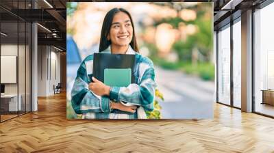 Young latin student girl smiling happy holding folder at the city. Wall mural