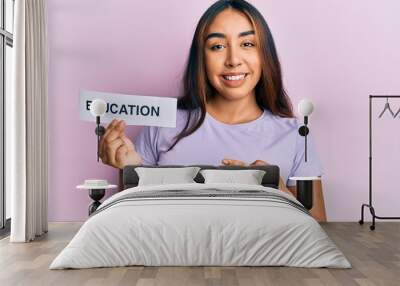 Young latin woman holding education word paper smiling happy pointing with hand and finger Wall mural