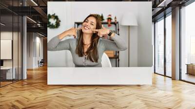 Young latin woman sitting on the table by christmas decor smiling cheerful showing and pointing with fingers teeth and mouth. dental health concept. Wall mural