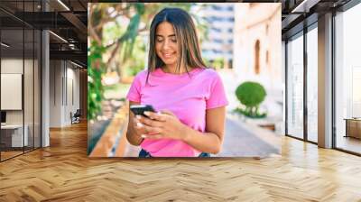 Young latin woman smiling happy using smartphone at the city. Wall mural