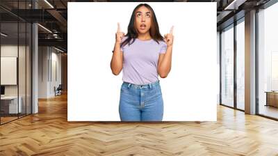 Young latin woman wearing casual clothes amazed and surprised looking up and pointing with fingers and raised arms. Wall mural