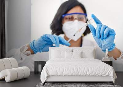 Young latin woman wearing scientist uniform and medical mask holding vaccine at laboratory Wall mural