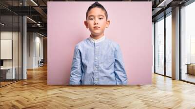 Young little boy kid wearing elegant shirt standing over pink isolated background with serious expression on face. Simple and natural looking at the camera. Wall mural