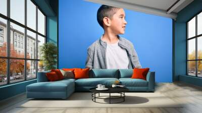 Young little boy kid wearing sport sweatshirt over blue isolated background looking away to side with smile on face, natural expression. Laughing confident. Wall mural