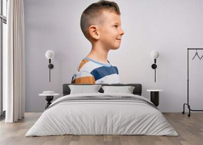 Young little caucasian kid with blue eyes standing wearing striped shirt over isolated background looking to side, relax profile pose with natural face with confident smile. Wall mural