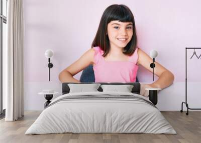 Young little girl with bang wearing casual clothes sitting on the table looking positive and happy standing and smiling with a confident smile showing teeth Wall mural