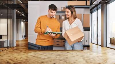 Young man and woman ecommerce business workers writing on book holding package at office Wall mural