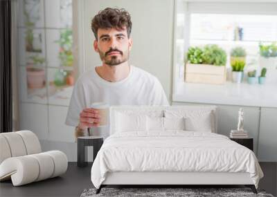 Young man drinking a coffee in a paper cup in the morning with a confident expression on smart face thinking serious Wall mural