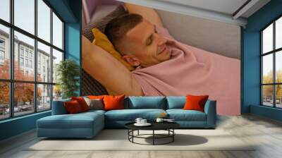 Young man relaxing on a couch in a cozy living room at home, enjoying a peaceful moment indoors in comfortable casual attire Wall mural