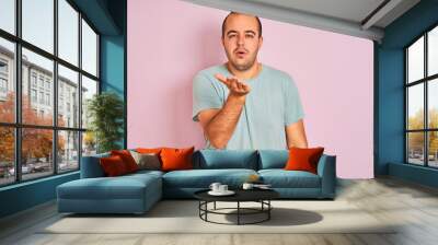 Young man wearing blue casual t-shirt standing over isolated pink background looking at the camera blowing a kiss with hand on air being lovely and sexy. Love expression. Wall mural