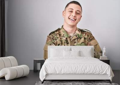 Young man wearing camouflage army uniform happy face smiling with crossed arms looking at the camera. positive person. Wall mural