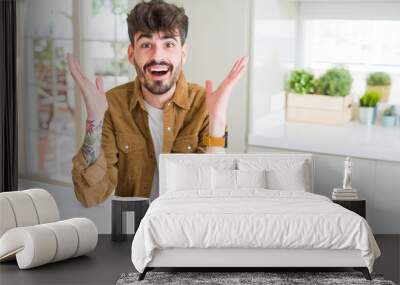 Young man wearing casual jacket sitting on white table celebrating crazy and amazed for success with arms raised and open eyes screaming excited. Winner concept Wall mural