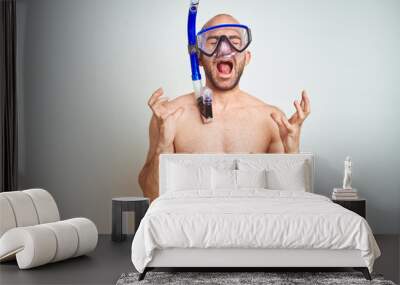 Young man wearing diving snorkel goggles equipent over isolated background celebrating mad and crazy for success with arms raised and closed eyes screaming excited. Winner concept Wall mural