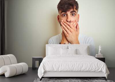 Young man with tattoo wearing t-shirt standing over isolated white background shocked covering mouth with hands for mistake. Secret concept. Wall mural