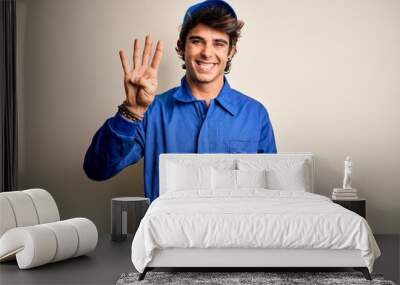 Young mechanic man wearing blue cap and uniform standing over isolated white background showing and pointing up with fingers number four while smiling confident and happy. Wall mural