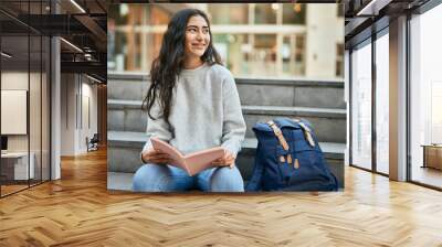 Young middle east student girl smiling happy reading book at the university. Wall mural