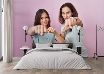 Young mother and daughter standing over pink background punching fist to fight, aggressive and angry attack, threat and violence Wall mural