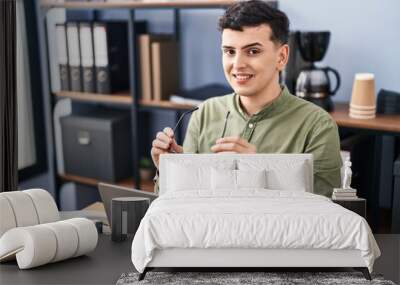 Young non binary man business worker holding glasses using laptop at office Wall mural