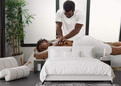 Young physiotherapist man smiling happy giving back massage to african american woman at the clinic. Wall mural