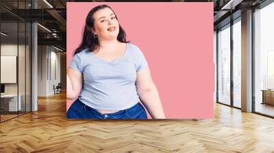 Young plus size woman wearing casual clothes smiling with happy face looking and pointing to the side with thumb up. Wall mural