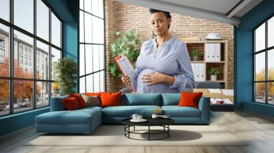 Young pregnant woman business worker touching belly holding clipboard at office Wall mural