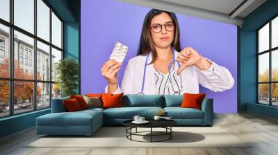 young professional doctor woman holding pharmaceutical pills over purple background with angry face, Wall mural