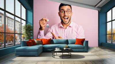 Young real estate business man holding new house keys over pink background very happy pointing with hand and finger Wall mural