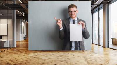 Young redhead  business man over grey grunge wall holding blank paper contract very happy pointing with hand and finger to the side Wall mural