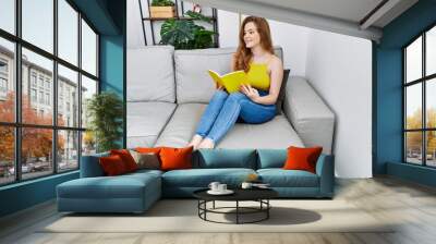 Young redhead girl smiling happy reading book at home Wall mural