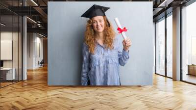 Young redhead graduated woman over grey grunge wall holding diploma with a happy face standing and smiling with a confident smile showing teeth Wall mural