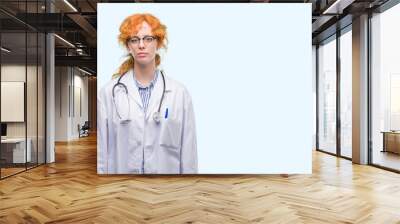 Young redhead woman wearing doctor uniform with serious expression on face. Simple and natural looking at the camera. Wall mural