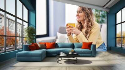 Young woman drinking coffee sitting on sofa at home Wall mural