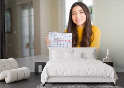 Young woman holding menstruation calendar with a happy face standing and smiling with a confident smile showing teeth Wall mural