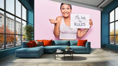 Young woman holding my body my rules banner screaming proud, celebrating victory and success very excited with raised arm Wall mural